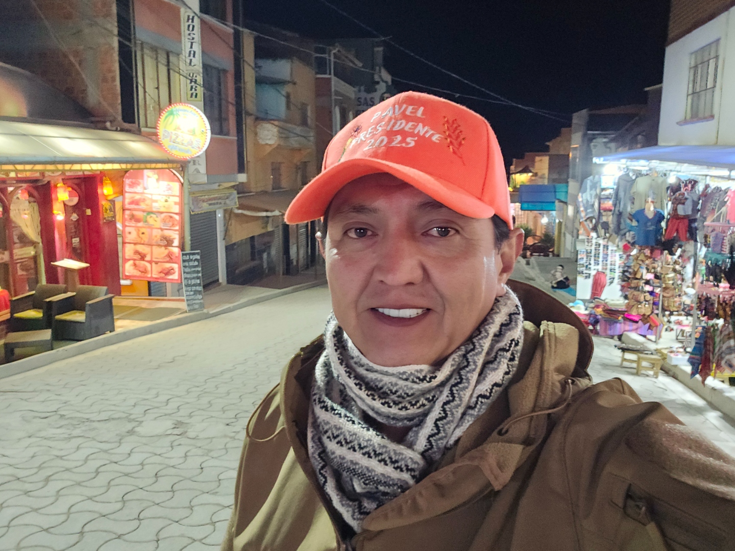 Pavel Aracena con gorra de la campaña Pavel Presidente 2025, en una calle de un pueblo boliviano por la noche